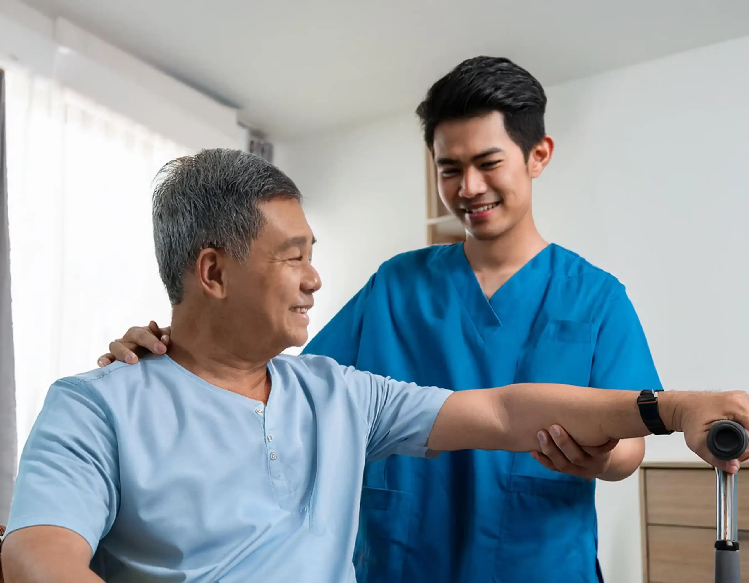 Healthcare professional in blue medical scrubs assisting older patient with rehabilitation exercise supporting arm extension in clinical or home setting with soft lighting and neutral walls representing physical therapy and supportive patient care